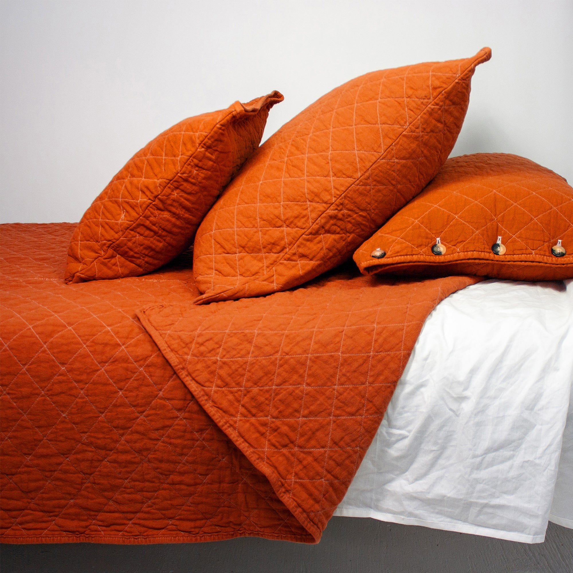 Orange quilted bedspread with matching pillows on a bed against a white background