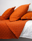 Orange quilted bedspread with matching pillows on a bed against a white background