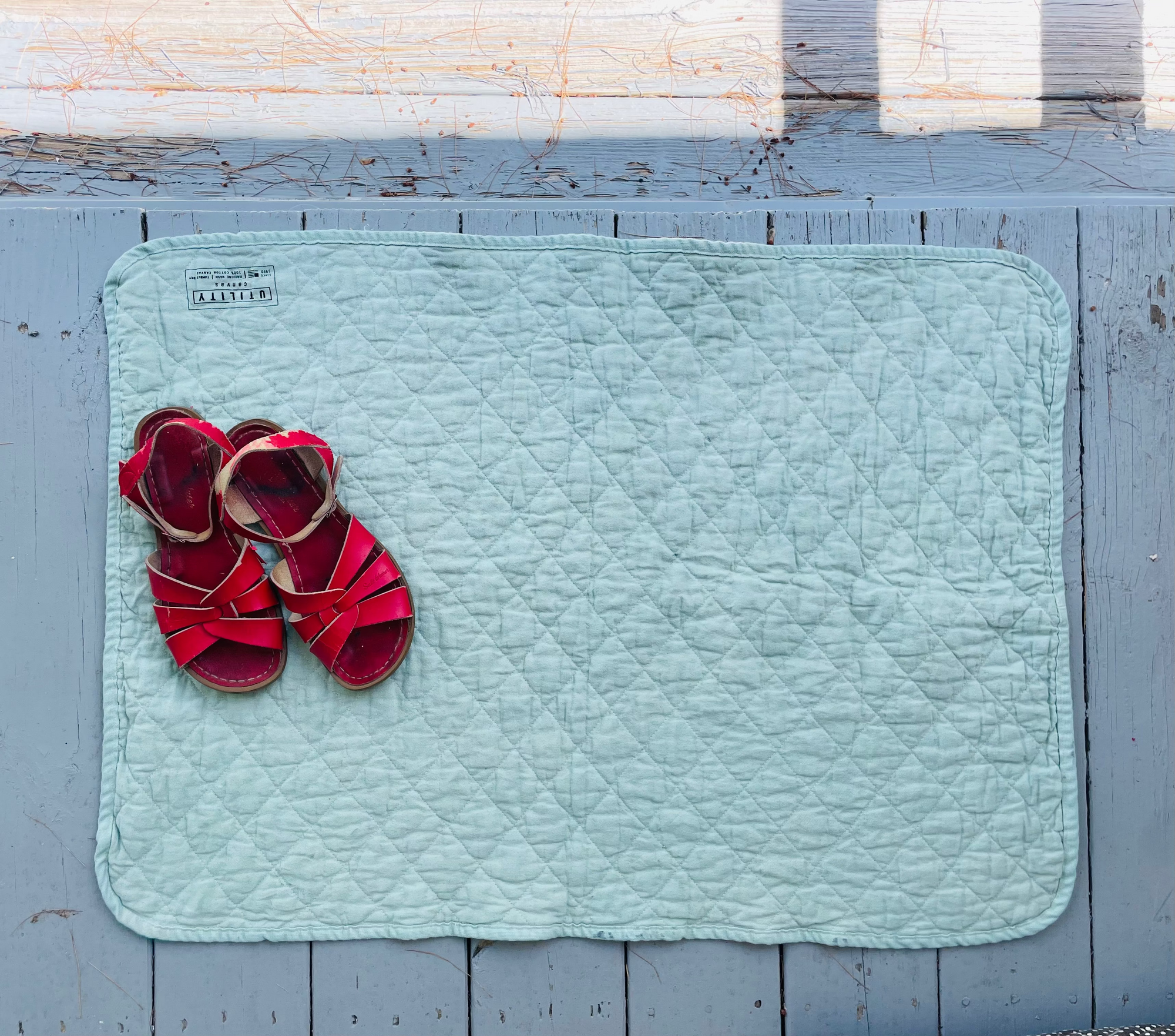 Red sandals on a light blue doormat with a wooden floor background