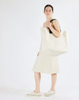 Woman holding a large white tote bag against a plain background