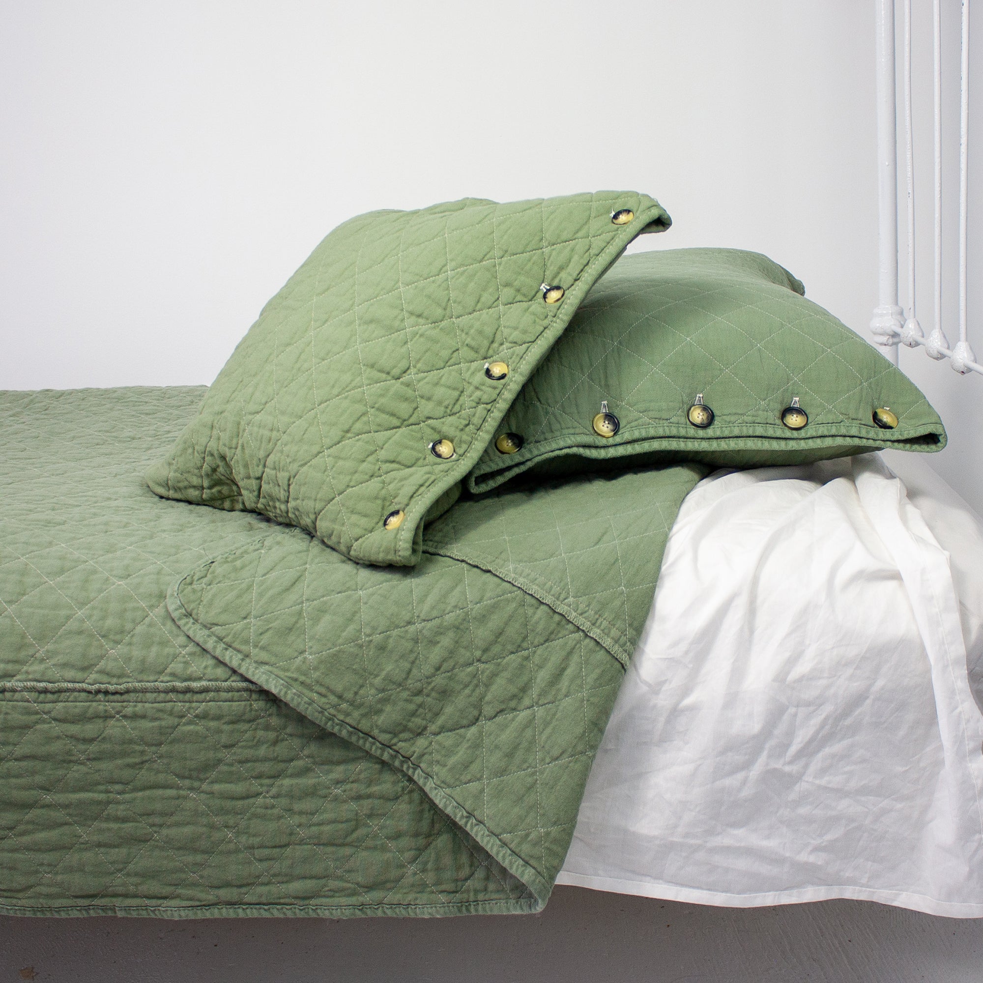 A green quilted coverlet with a diamond pattern laid out on a bed, accompanied by matching green pillows with visible buttons.
