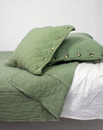A green quilted coverlet with a diamond pattern laid out on a bed, accompanied by matching green pillows with visible buttons.