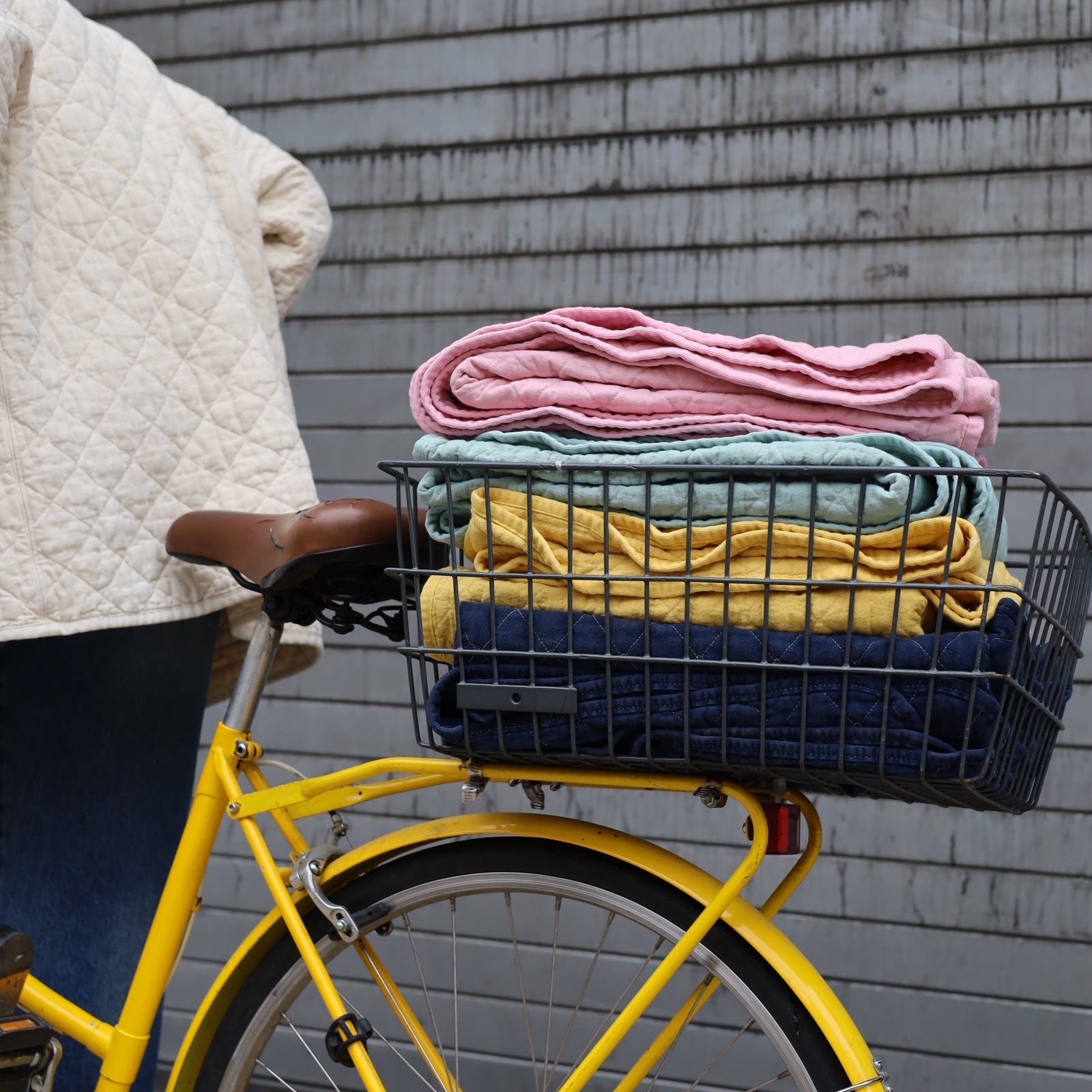 Yellow bicycle with a basket containing folded clothes on a wooden deck.