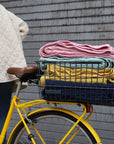 Yellow bicycle with a basket containing folded clothes on a wooden deck.